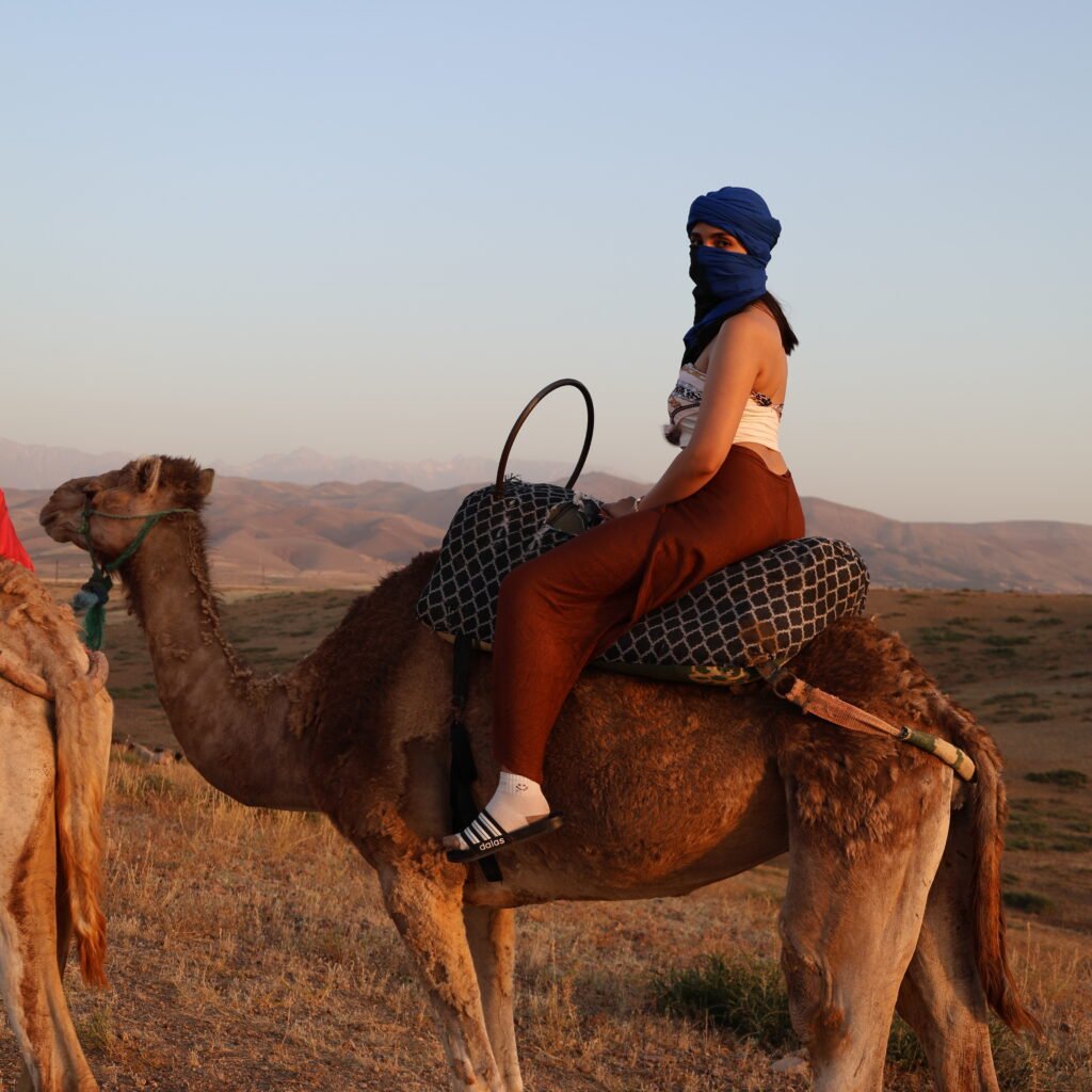 Female traveler wearing a blue headscarf riding a camel in the Moroccan desert