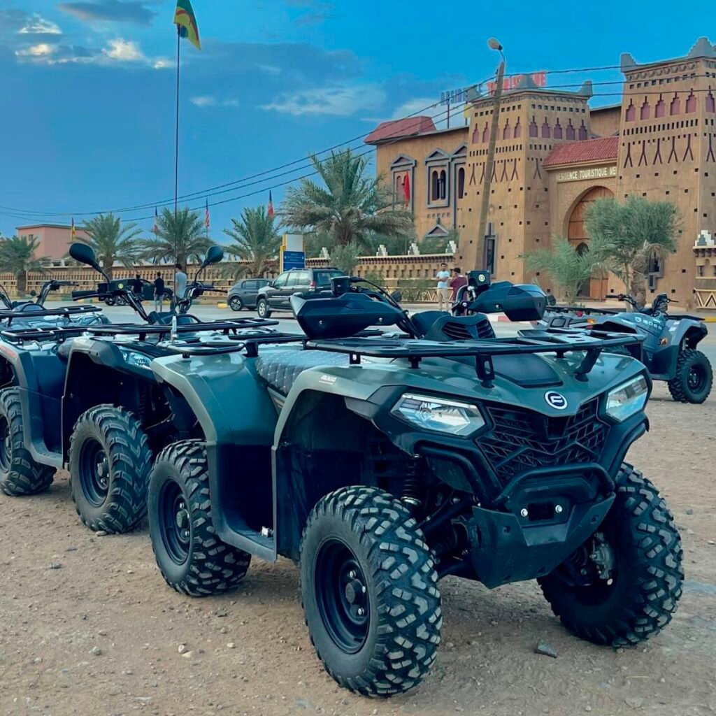 A fleet of green quad bikes parked in a line outside traditional Moroccan architecture under a blue sky