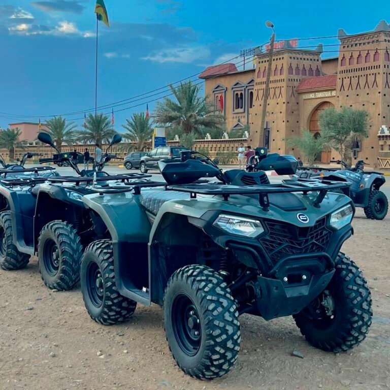 A fleet of green quad bikes parked in a line outside traditional Moroccan architecture under a blue sky