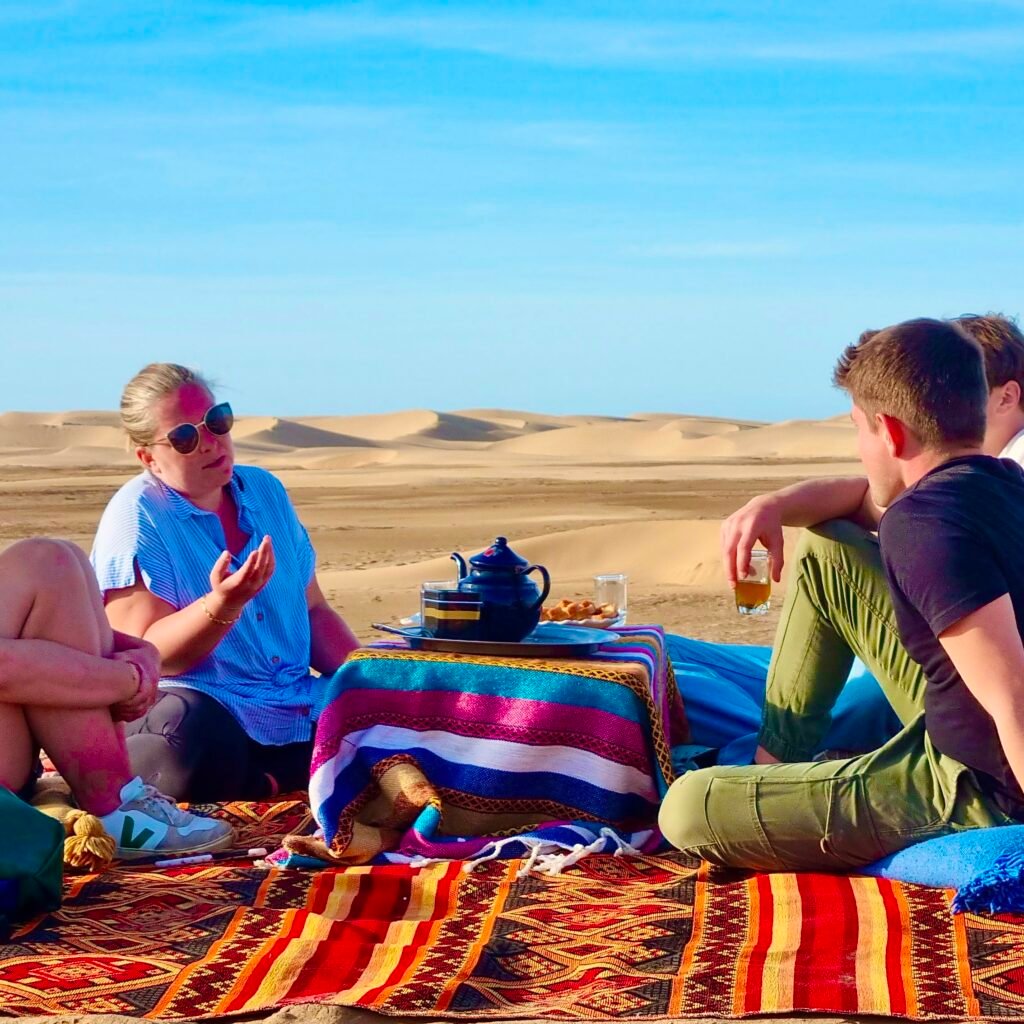 A group of travelers sitting on traditional rugs enjoying tea in the Sahara desert