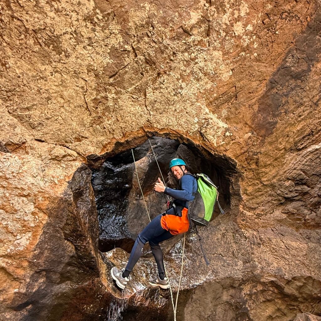 Adventurer rappelling near waterfall cave.