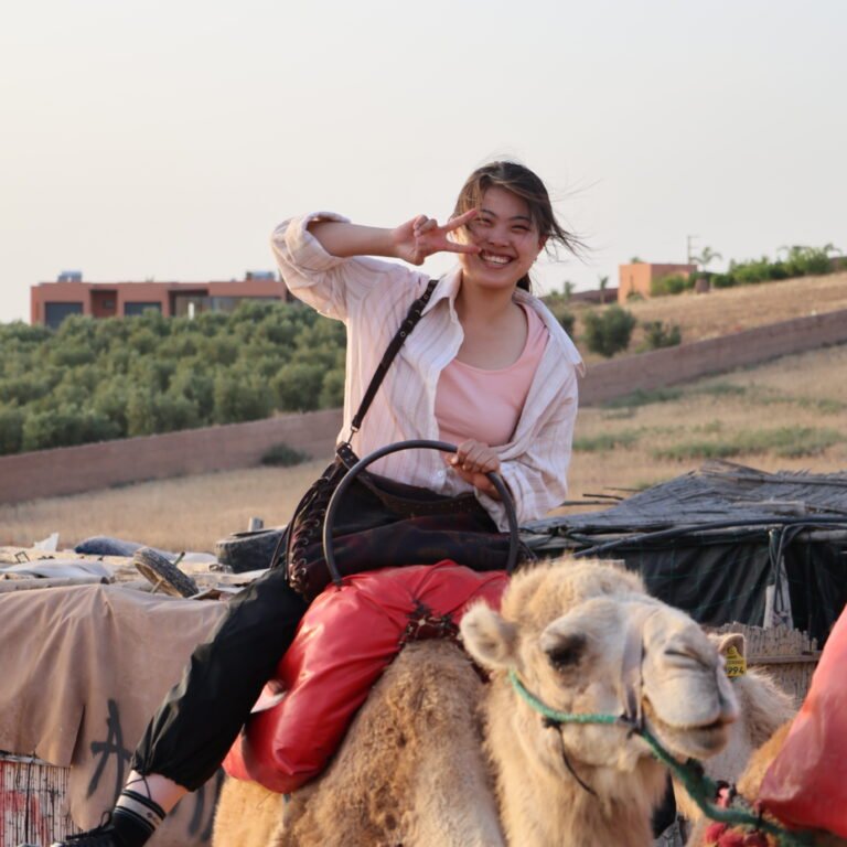 Smiling female traveler riding a camel during a sunset desert tour in Morocco