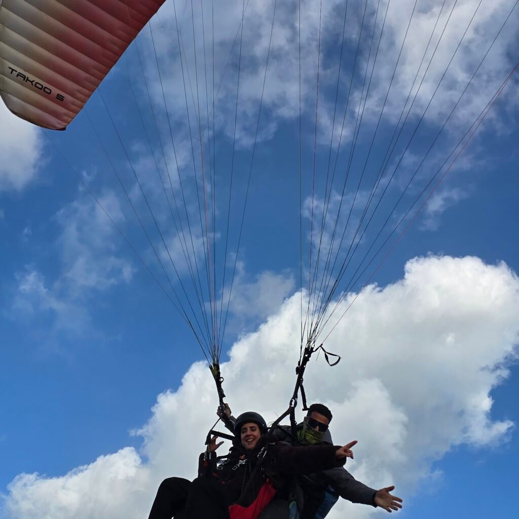 Tandem paraglider flying against a blue sky with a red canopy overhead