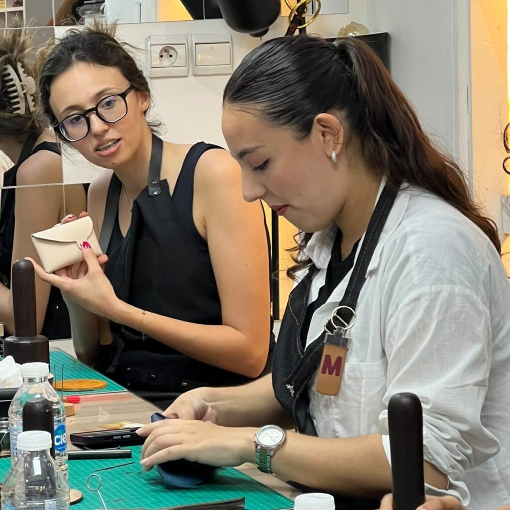 Woman assembling a handmade leather pouch while an instructor assists during a class