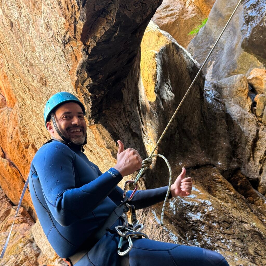 Traveler giving thumbs-up gestures while rappelling through a natural stone arch in Morocco