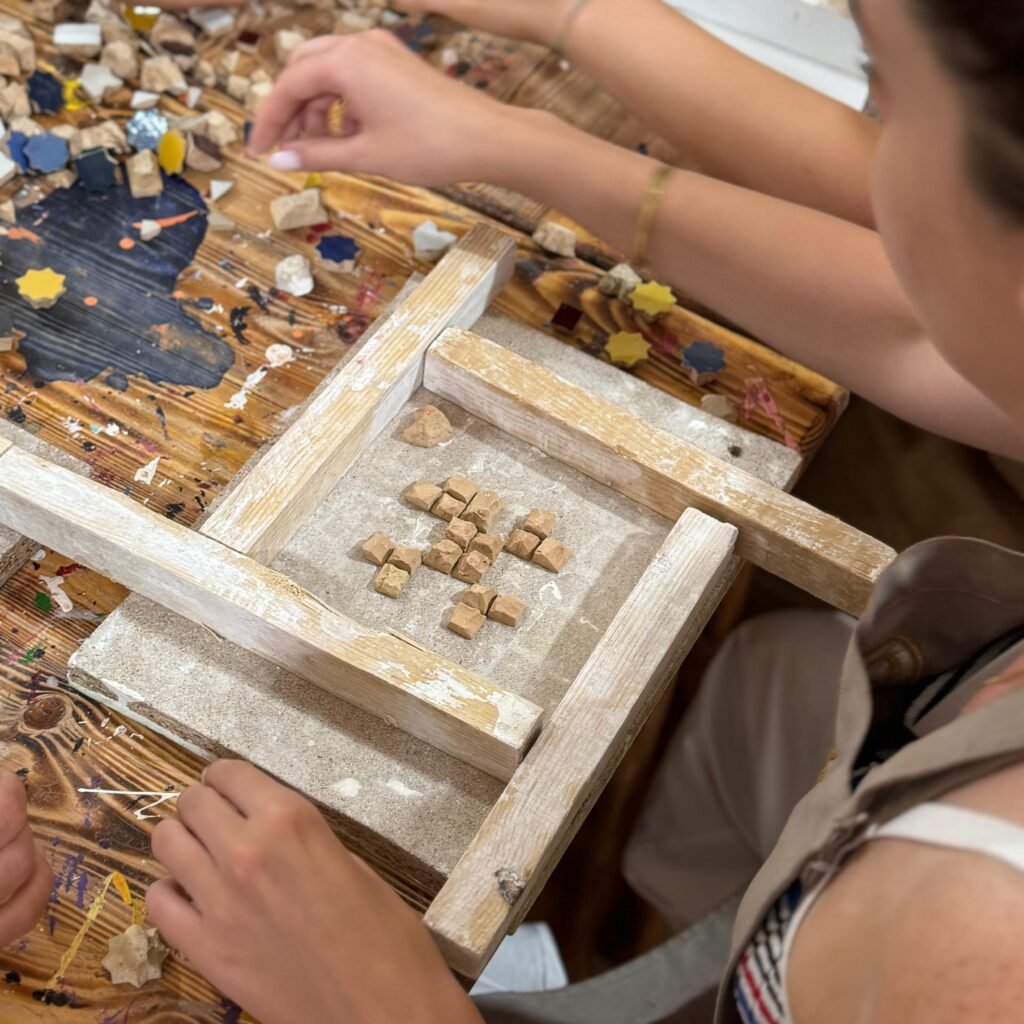Close-up of hands arranging geometric zellij clay tile pieces into a pattern
