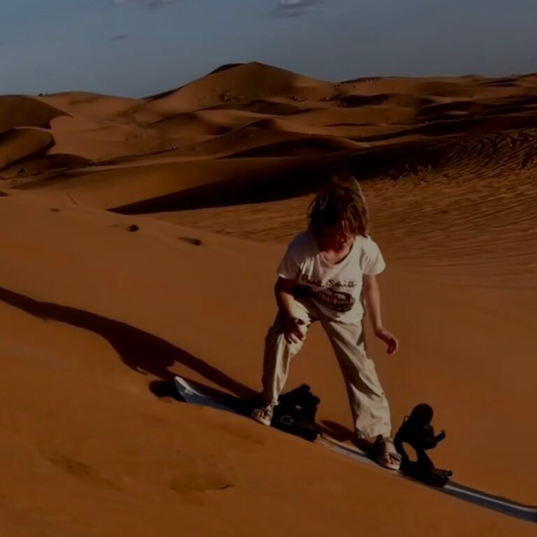 Person preparing to sandboard down golden desert sand dunes