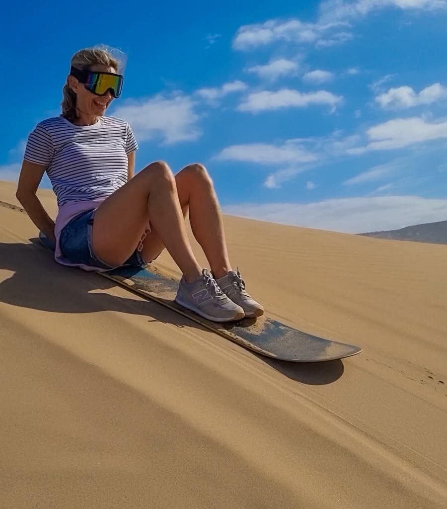 Female traveler enjoying sandboarding down sand dunes during a Sahara desert tour