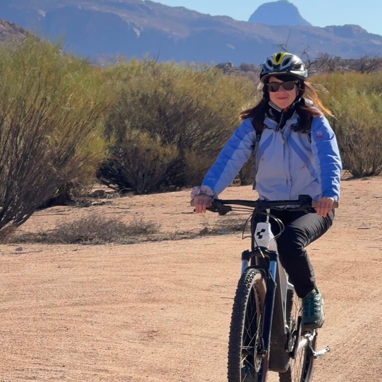 Female traveler wearing a helmet riding a bicycle along a dirt trail with mountains in Tafraoute, Morocco