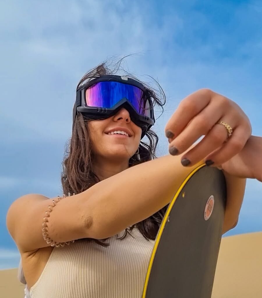Female traveler posing with a sandboard on a desert dune during a Sahara sandboarding tour