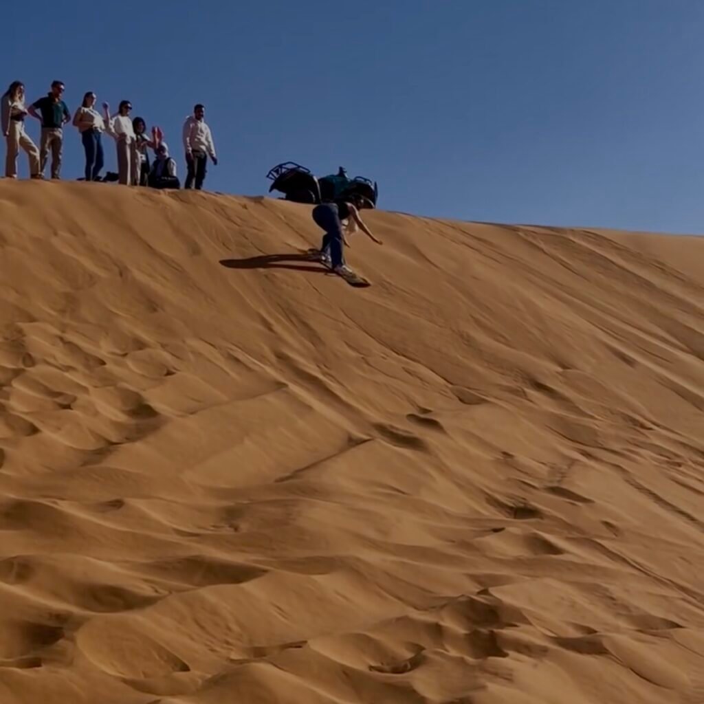 Group watching a person sandboarding down a steep desert dune