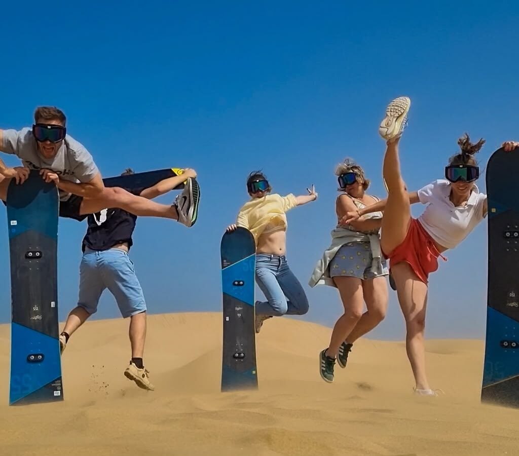 Group of adventurous travelers posing with sandboards during a Sahara desert sandboarding excursion