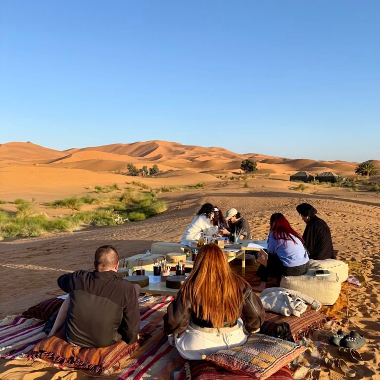 Group of people seated outdoors on traditional rugs and cushions in the Sahara Desert, participating in a workshop surrounded by sand dunes