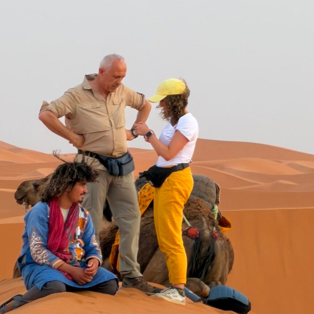Group of travelers interacting with a local guide beside a camel in the Sahara desert