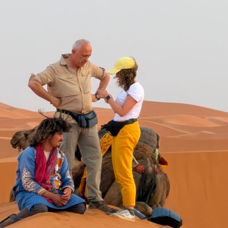Group of travelers interacting with a local guide beside a camel in the Sahara desert