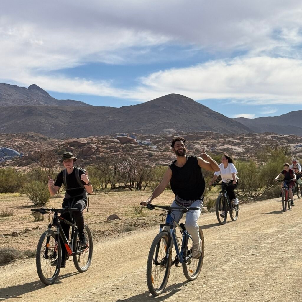 Group of travelers cycling along a gravel road surrounded by desert hills in Tafraoute, Morocco