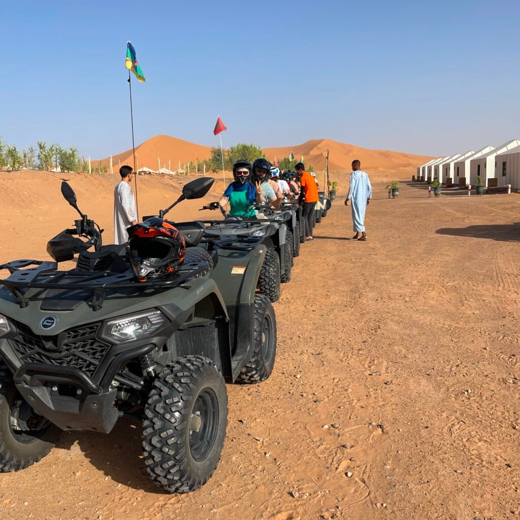 Group of travelers on quad bikes lined up outside desert camp tents in the Sahara