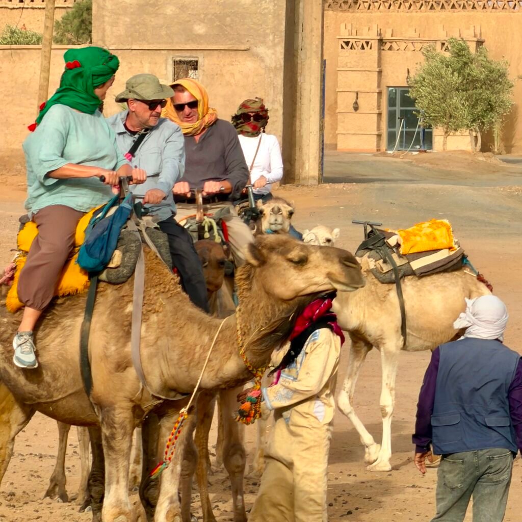 Group of travelers preparing to ride camels through a desert village on a Sahara tour