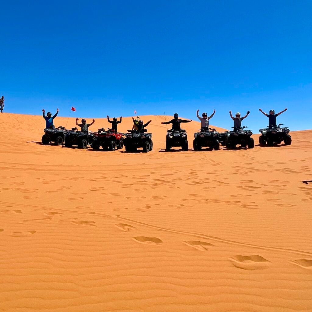 Group of travelers raising their arms on quad bikes during a Sahara desert sand dune tour