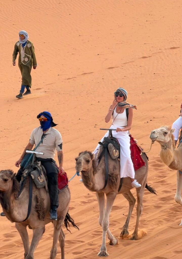 Group of travelers riding camels across the Sahara desert dunes with a local Moroccan guide