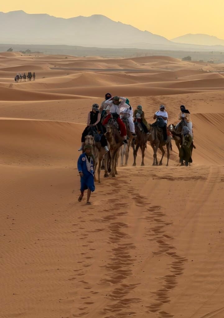 Group of travelers riding camels in a caravan across the Sahara desert dunes