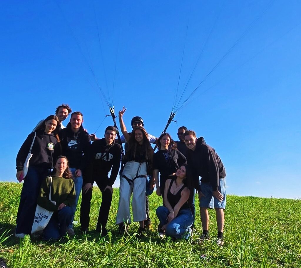 Group of tour travelers posing beneath an open green paraglider canopy
