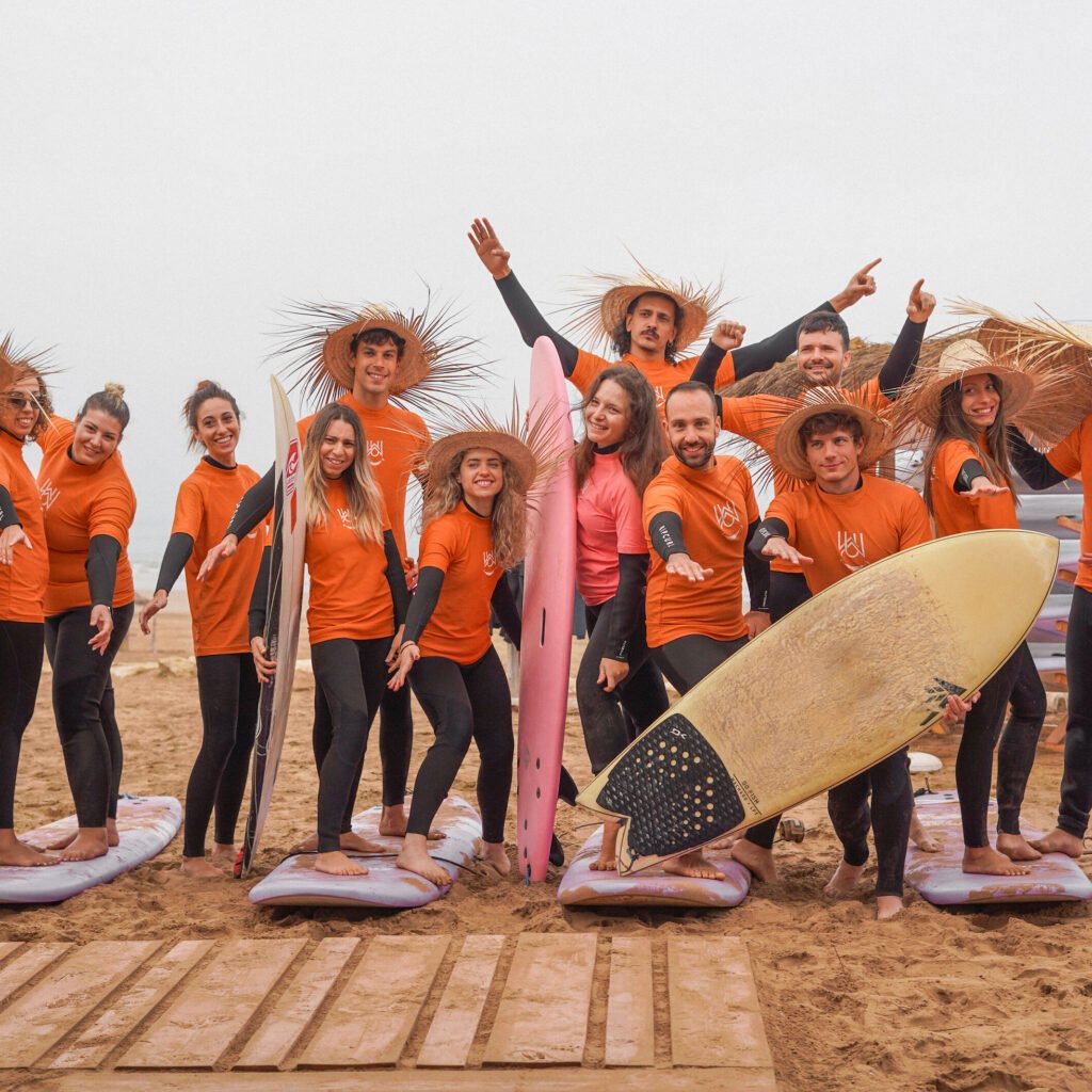 Group of surf camp participants posing together on the sandy beach with surfboards and straw hats