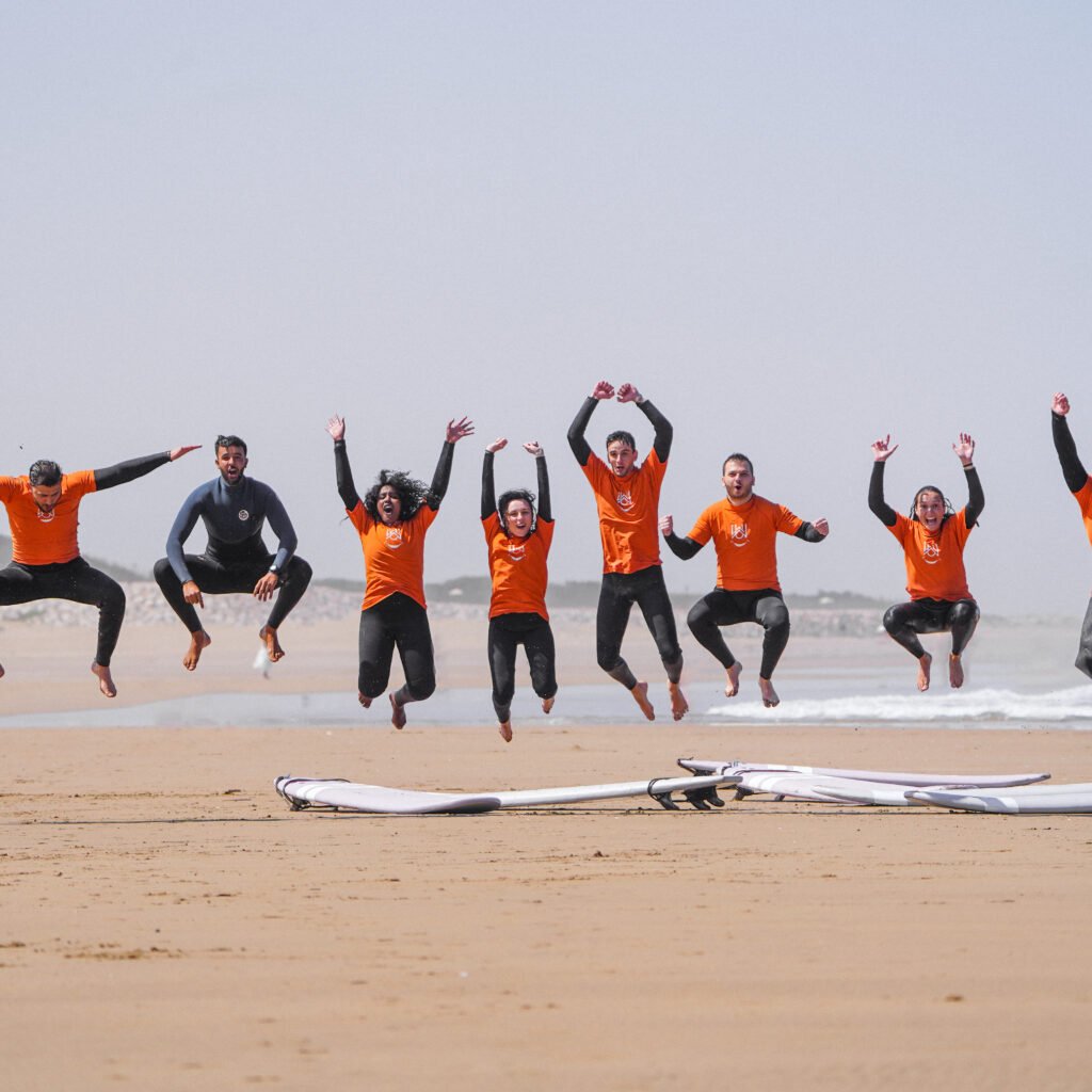 Group of surf camp students jumping in the air on the beach with surfboards lying on the sand