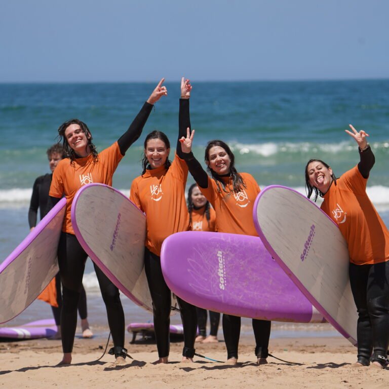 Row of surfers holding softtop surfboards upright on the sandy beach