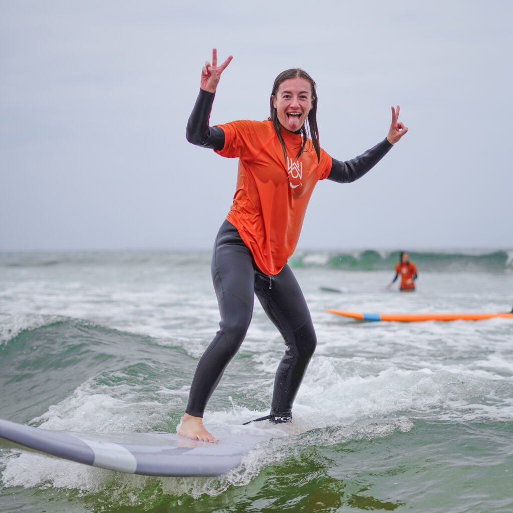 Smiling female surfer making peace signs while riding a wave on a surfboard