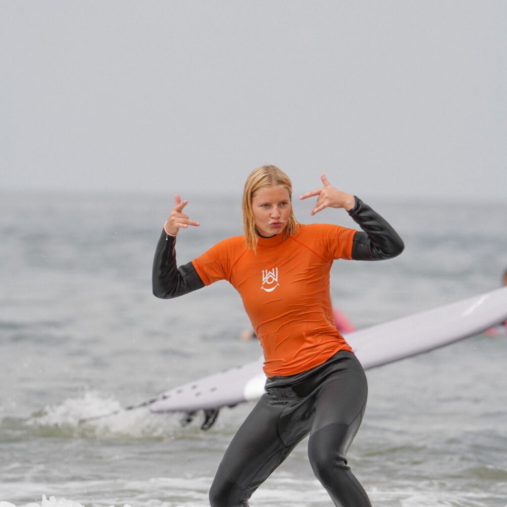 Female surfer posing playfully with shaka hand signs while riding a white surfboard
