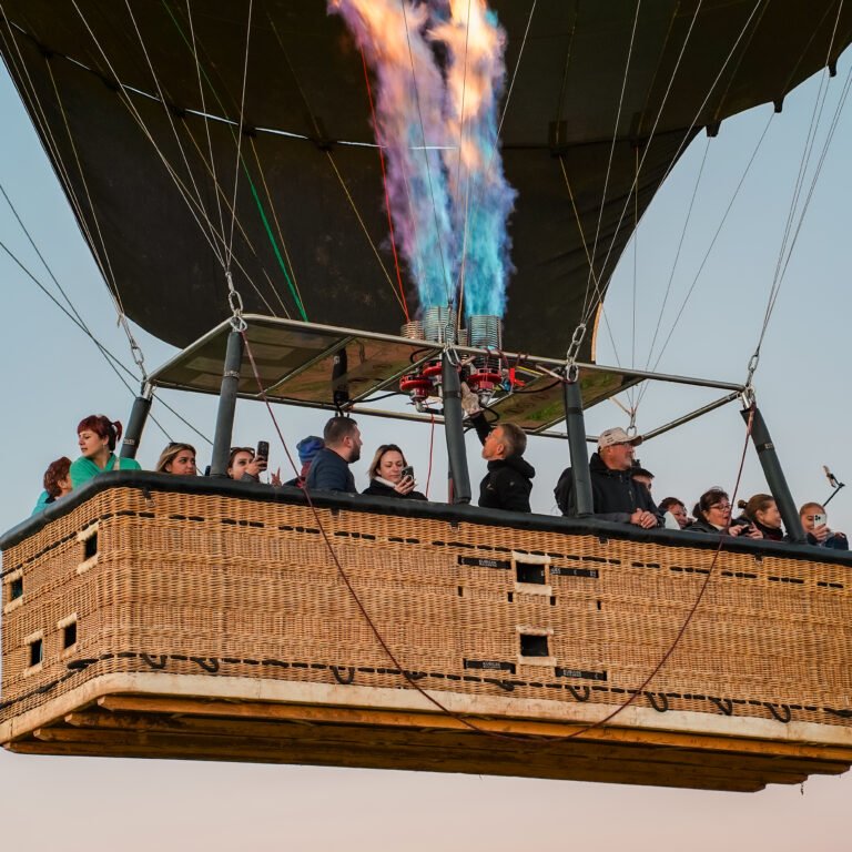 Passengers in a large wicker hot air balloon basket watching the burner fire a spectacular blue and orange flame into the envelope during a scenic flight.
