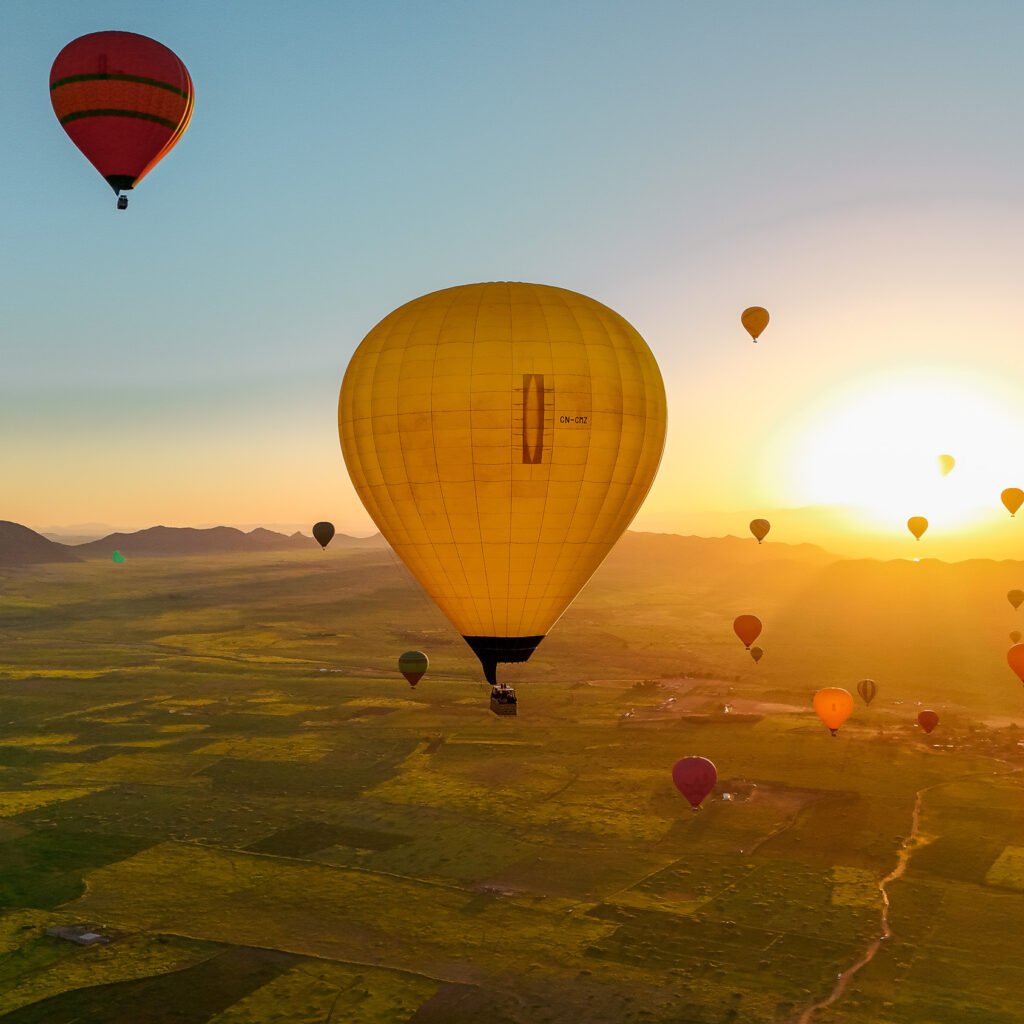 Yellow hot air balloon flying over green fields against a bright sunrise sky in Morocco