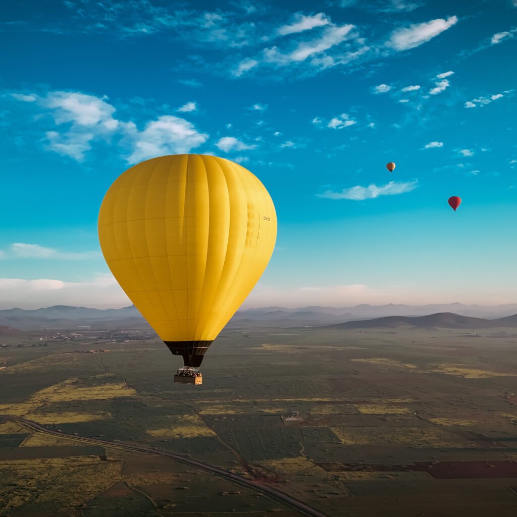 Bright yellow hot air balloon soaring above open landscapes and distant mountains under a blue sky in Morocco