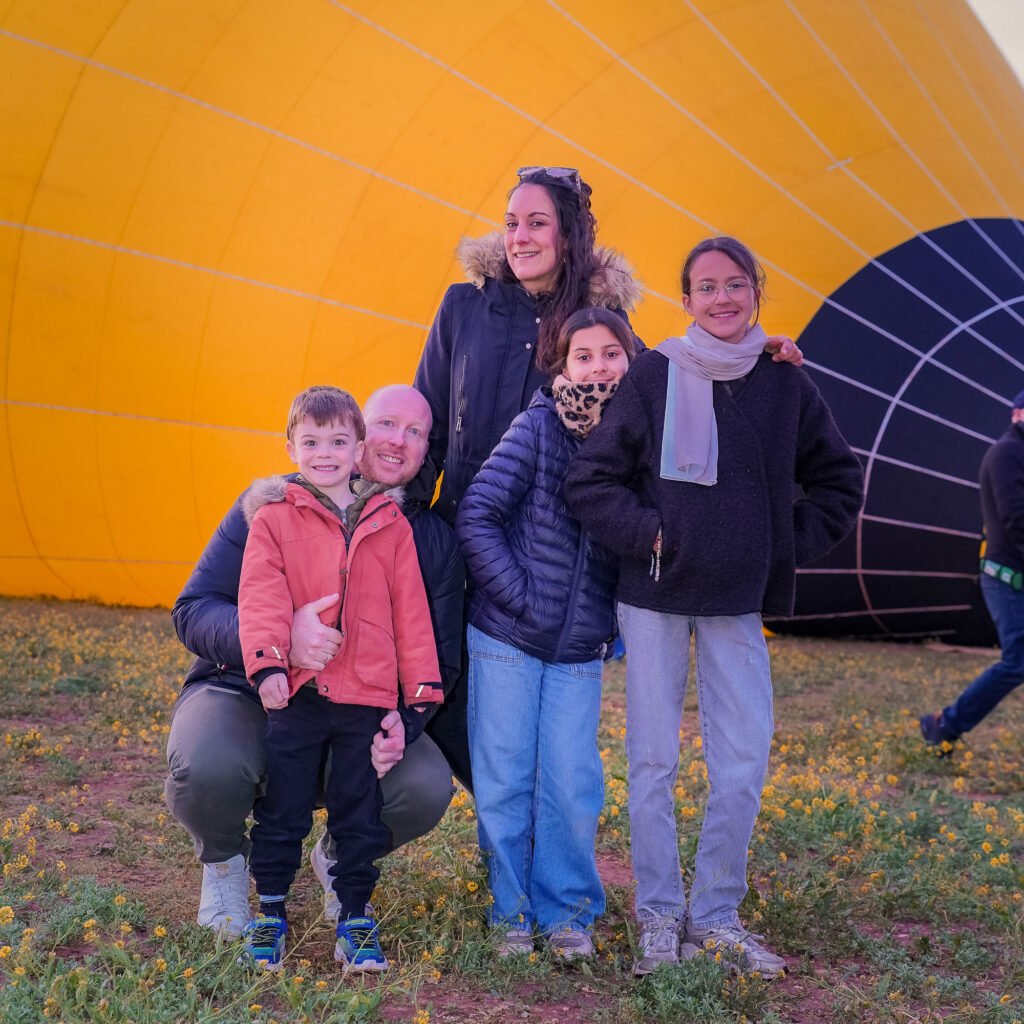 Happy family posing together in front of a giant yellow hot air balloon in Morocco
