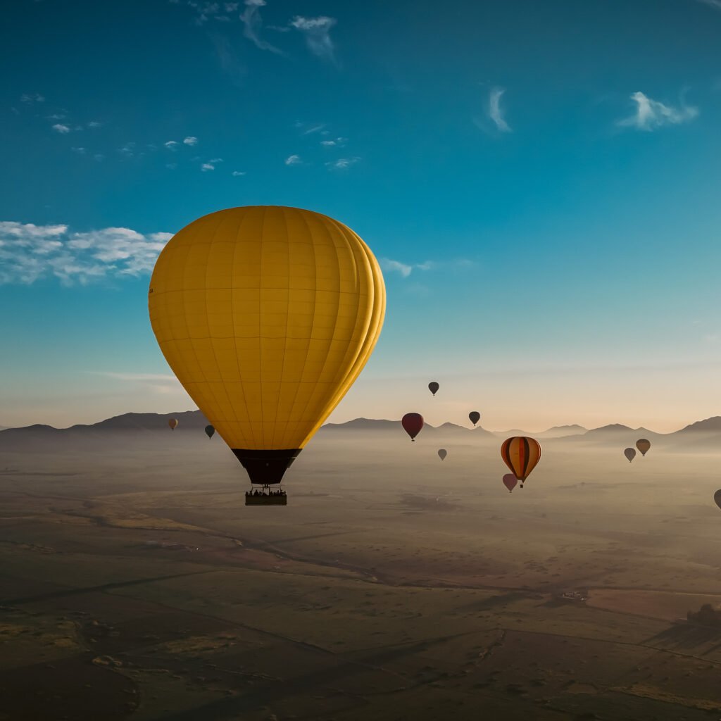 Bright yellow hot air balloon floating above misty desert landscape and mountain ranges at sunrise in Morocco