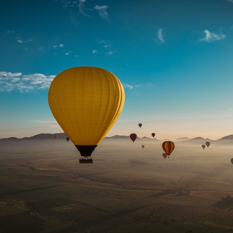 Bright yellow hot air balloon floating above misty desert landscape and mountain ranges at sunrise in Morocco
