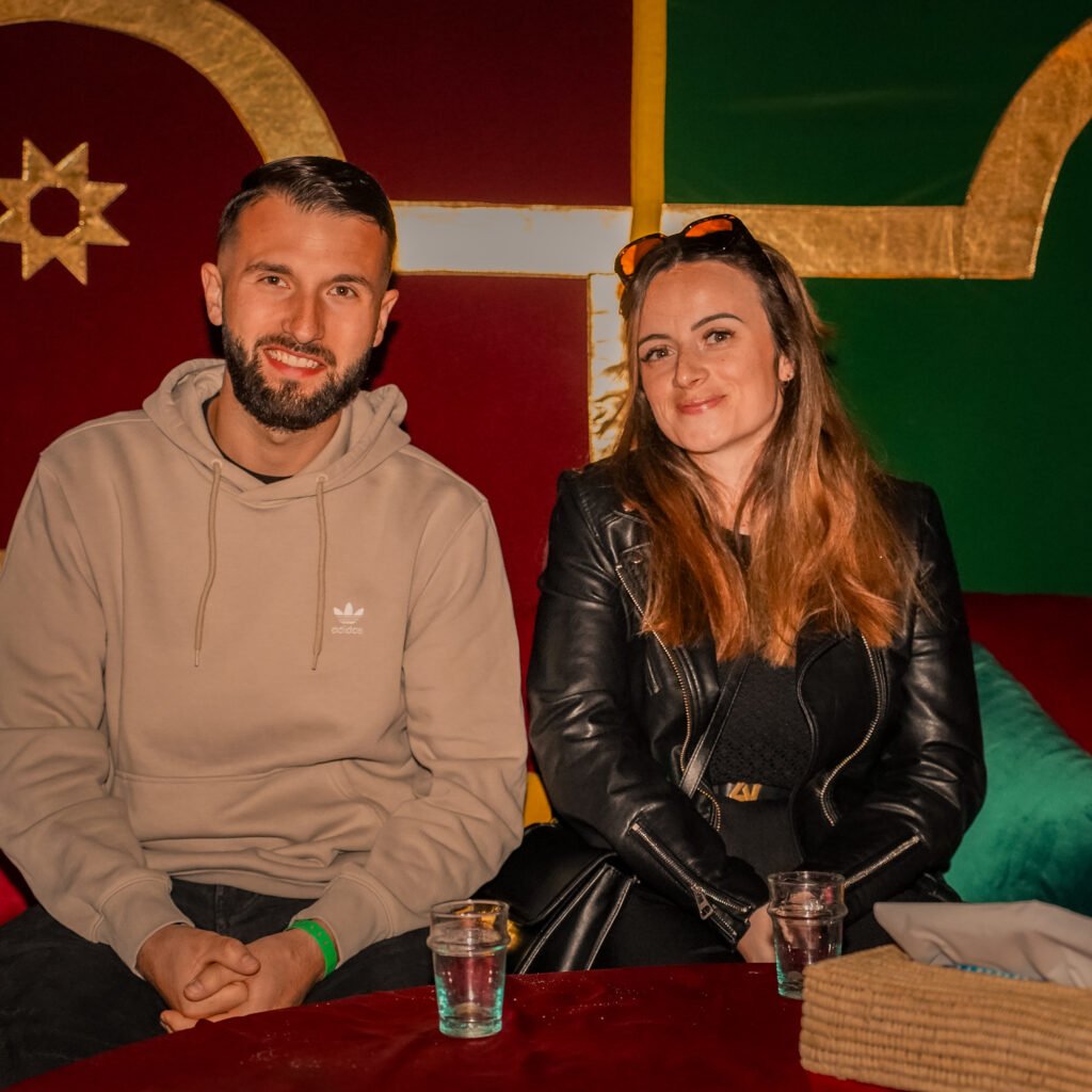 Couple sitting on red cushions inside a traditional Moroccan tent with decorative gold stars and colorful pillows after a hot air balloon ride.