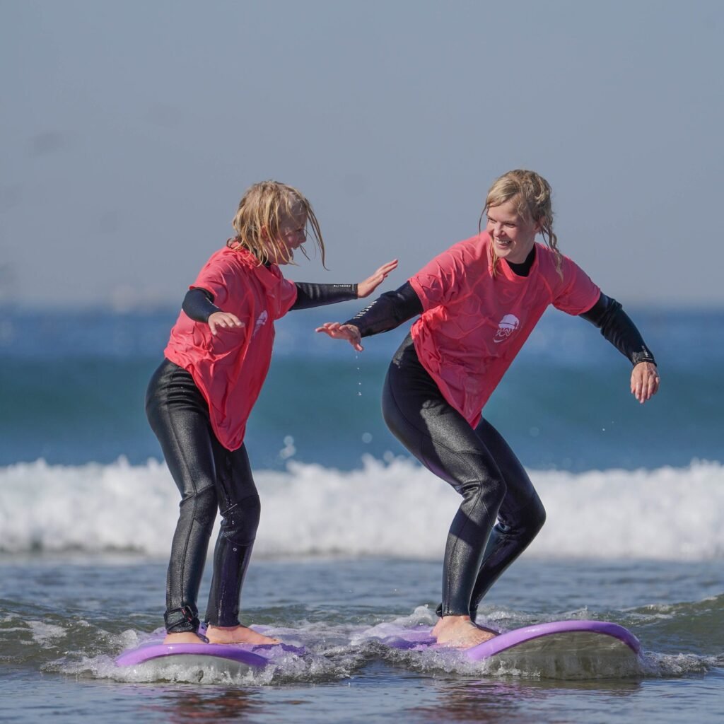 Adult and child surfing together side-by-side on softboard surfboards