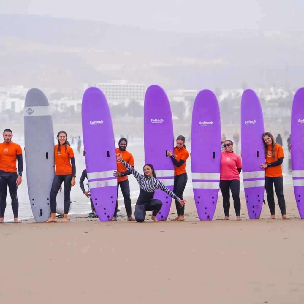 Group of surf students posing in a row on the beach with purple softboards