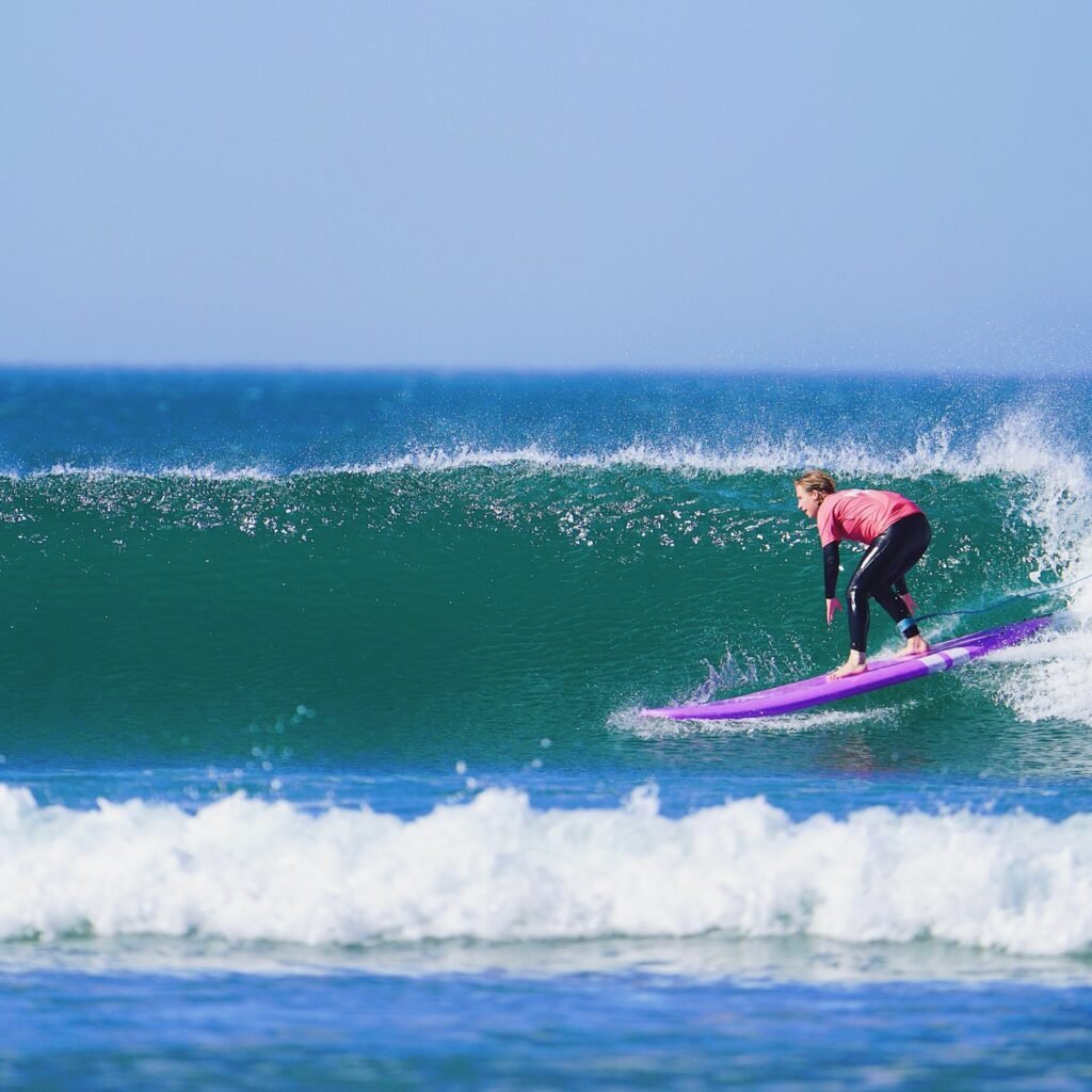 Surfer riding a purple surfboard along the face of a clean ocean wave