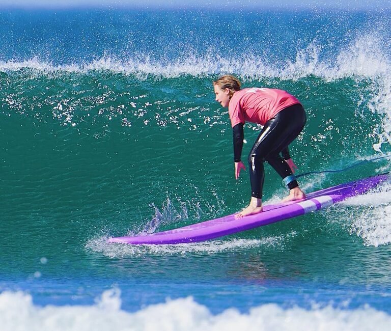 Surfer riding a purple surfboard along the face of a clean ocean wave