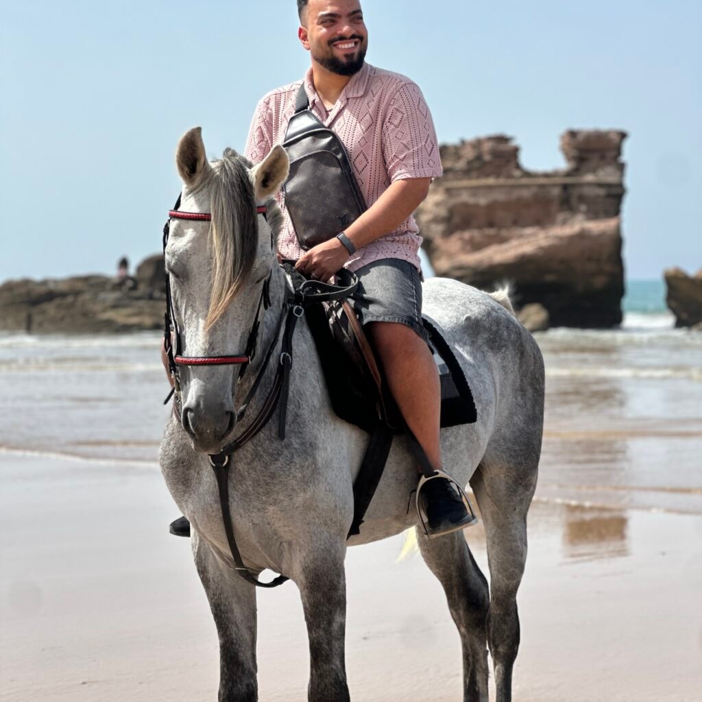 Smiling male traveler riding a white horse on the shoreline near historical coastal ruins