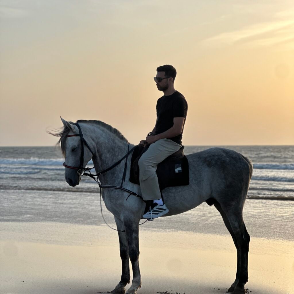Traveler riding a white horse along the ocean shoreline during sunset