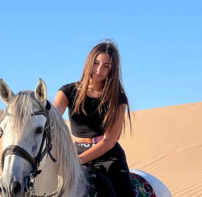 Young female traveler riding a white horse on desert sand dunes in Morocco