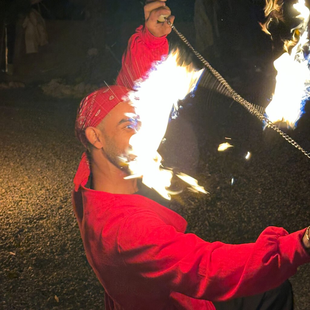 Fire performer with a red bandana and shirt demonstrating fire manipulation outdoors at night