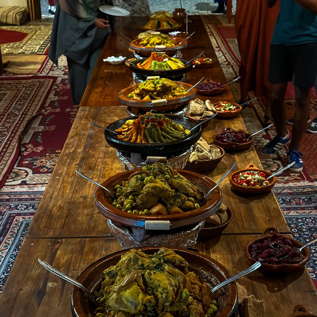 Long wooden buffet table laden with traditional Moroccan tagines, salads, and bread during an evening dinner event