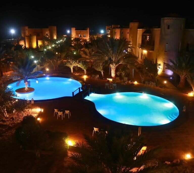 Illuminated outdoor swimming pools and palm trees at a Moroccan desert resort at night