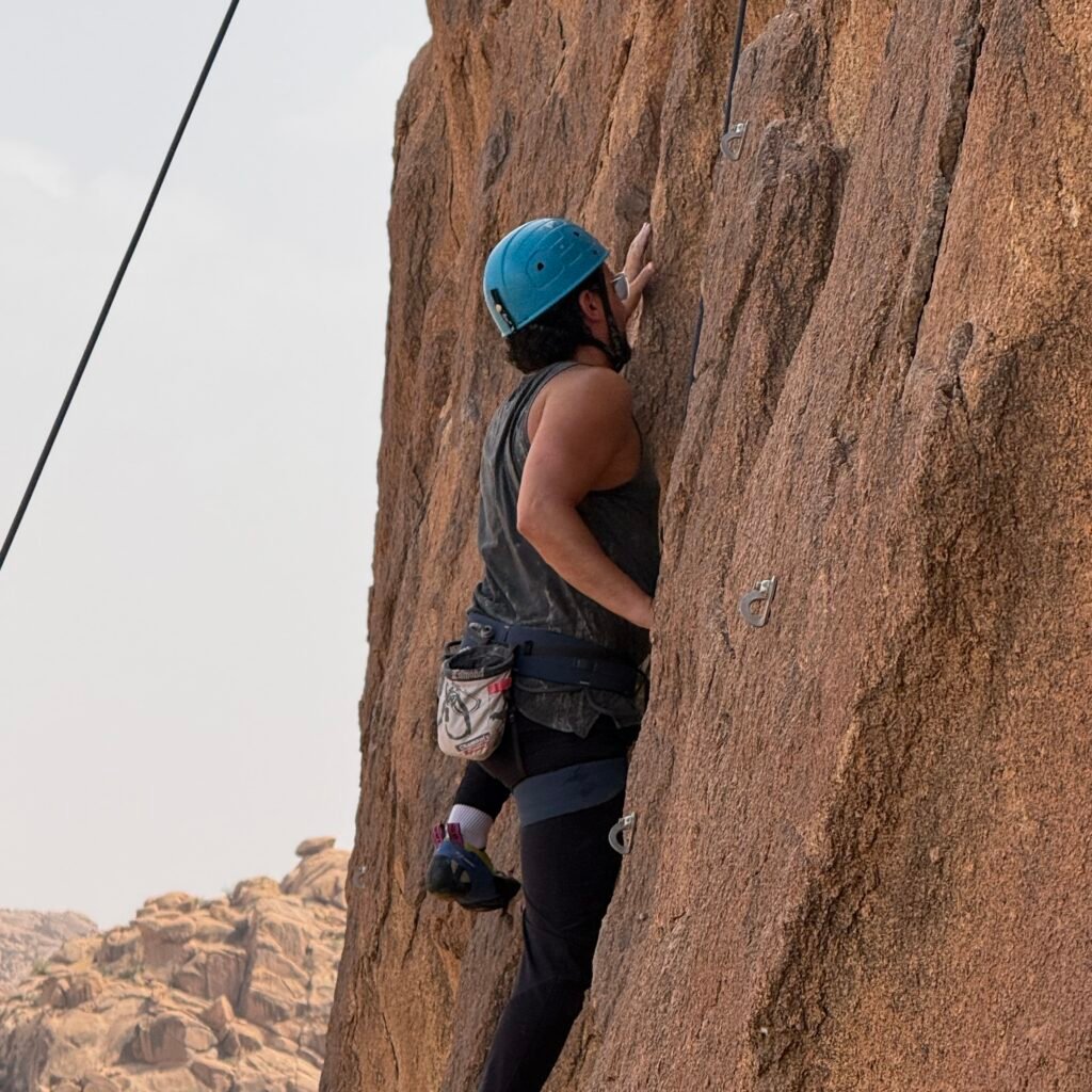Side view of a climber wearing a helmet scaling a steep granite rock wall in Morocco
