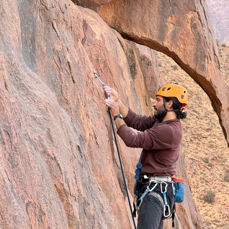 Climber clipping safety rope into a quickdraw anchor on a granite rock face in Morocco